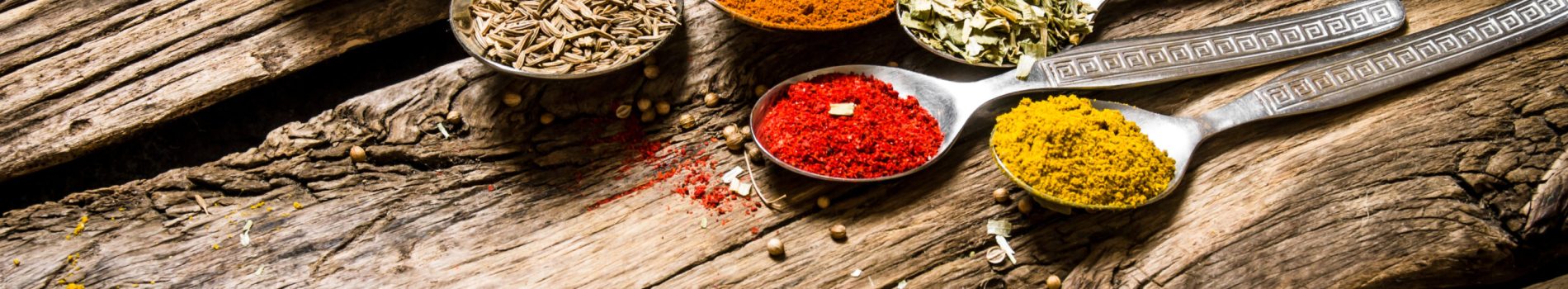 Different kinds of spices in spoons. On wooden background.